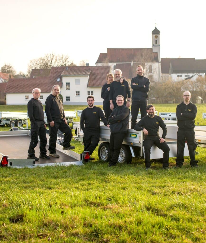 Team posiert auf Anhängern vor Dorfkulisse